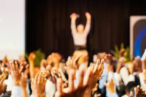 Hands raised to the sky with an out of focus human with arms raised in the background