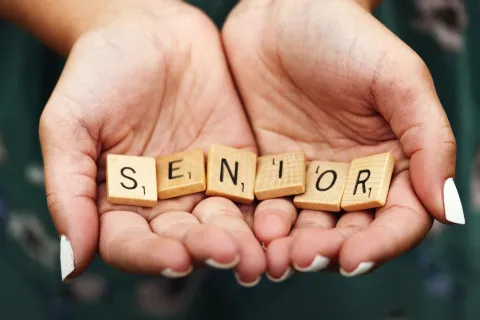Two hands holding word tiles that spell "Senior"