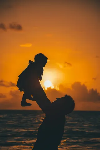 Father holding a child up with the sunset in the background