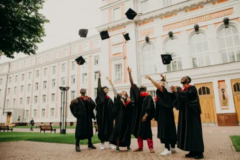 Students throwing graduation caps up in the air in front of a school