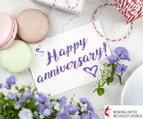 "Happy Anniversary" words on a white card surrounding macarons of different colors and purple flowers on a white table